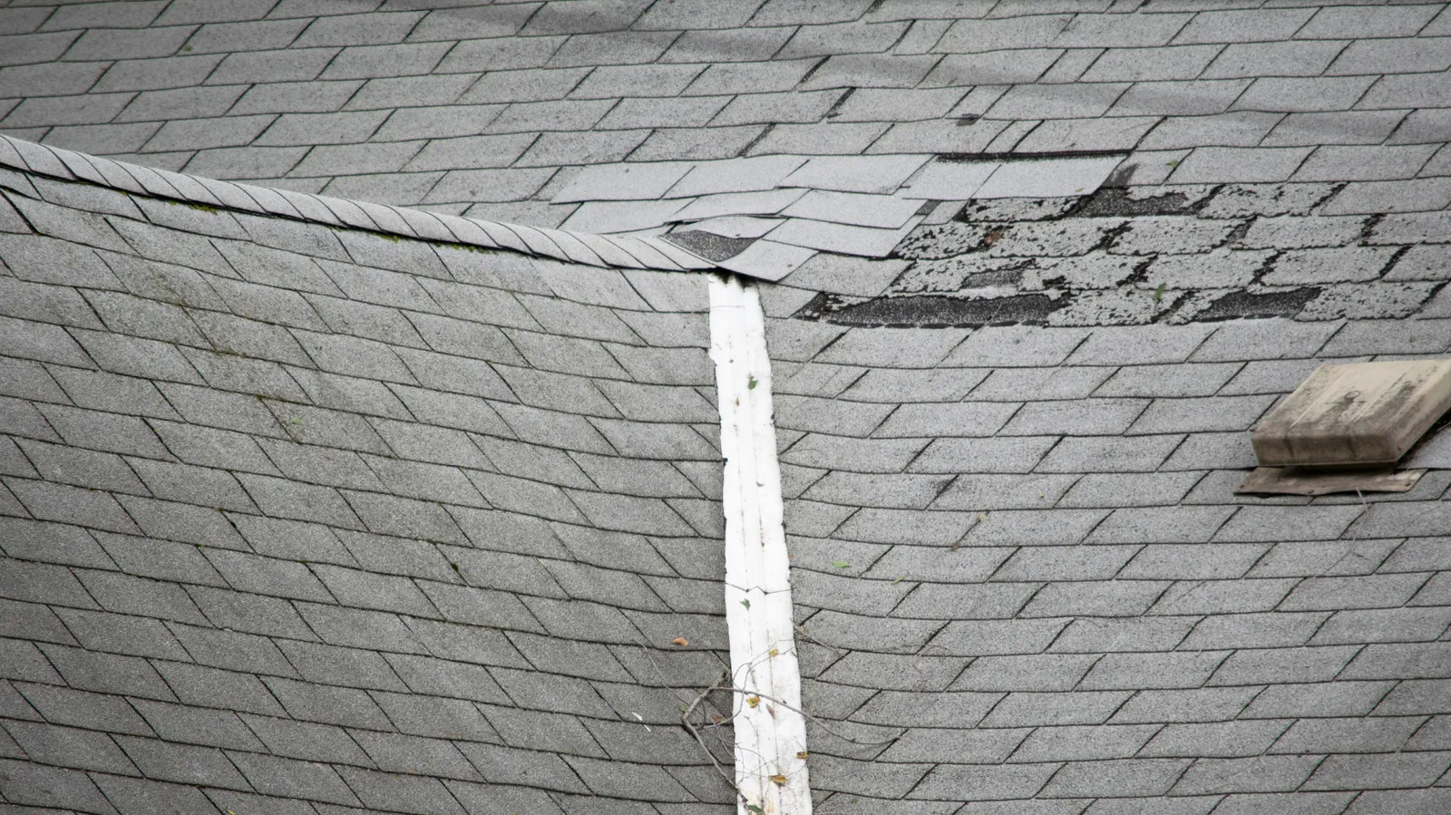Shingle tabs broken and creased across a weathered gray roof